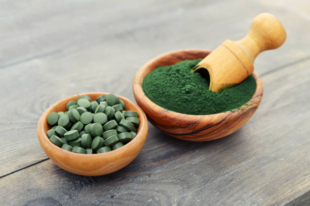 Green ground spirulina and spirulina powder in pills over black wooden background