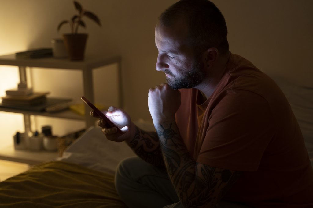 blue screen lights don't help you have a better sleep. Men with a smartphone producing blue light, one of the factors affecting sleep.