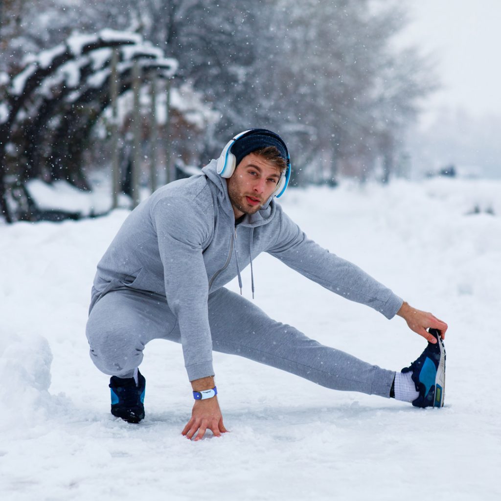 Man stretching his left leg under the snow after working out