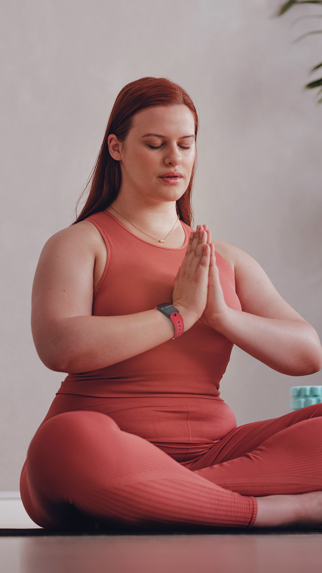 Woman doing yoga on the floor wearing a red GEMA Fitness Tracker