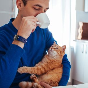 Man driking a cup of coffee with his cat in his arms wearing his blue GEMA Fitness Tracker